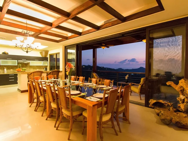 Dining table and kitchen at Villa Celaje with a sunset view through the open terrace wall